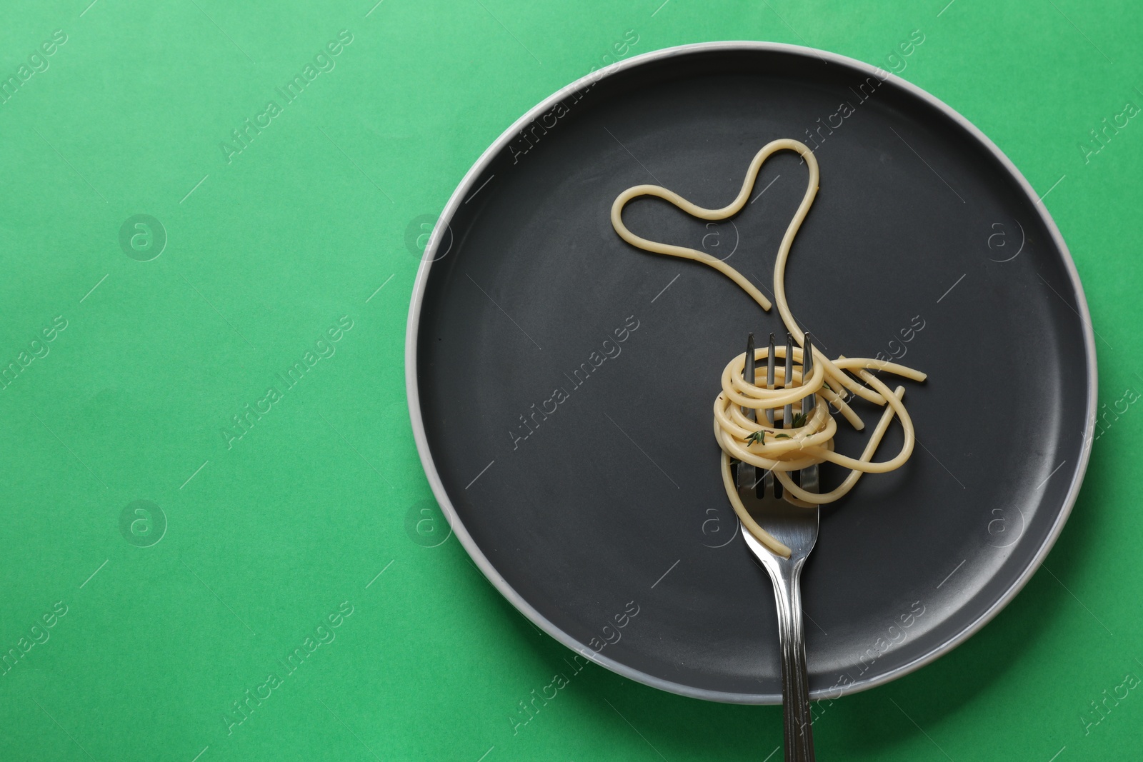 Photo of Heart made of tasty spaghetti and fork on green background, top view. Space for text