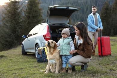 Photo of Mother with her daughter, dog and man near car in mountains. Family traveling with pet