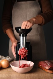 Woman making beef mince with electric meat grinder at wooden table, closeup