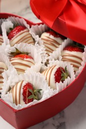 Heart shaped box with delicious chocolate covered strawberries on white marble table, closeup