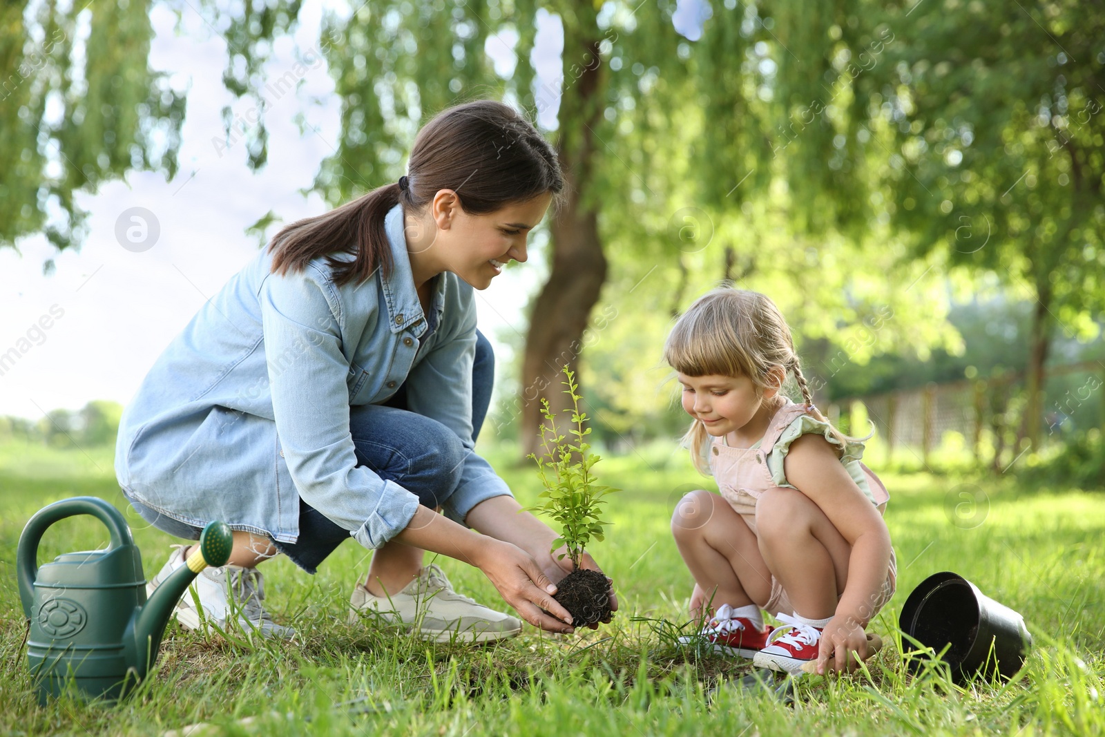 Photo of Mother and her daughter planting tree together in garden