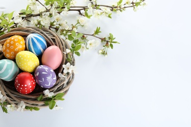 Photo of Painted Easter eggs in nest and blossoming branches on white background, top view