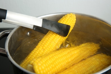 Taking fresh corn cob from pot with hot water on stove