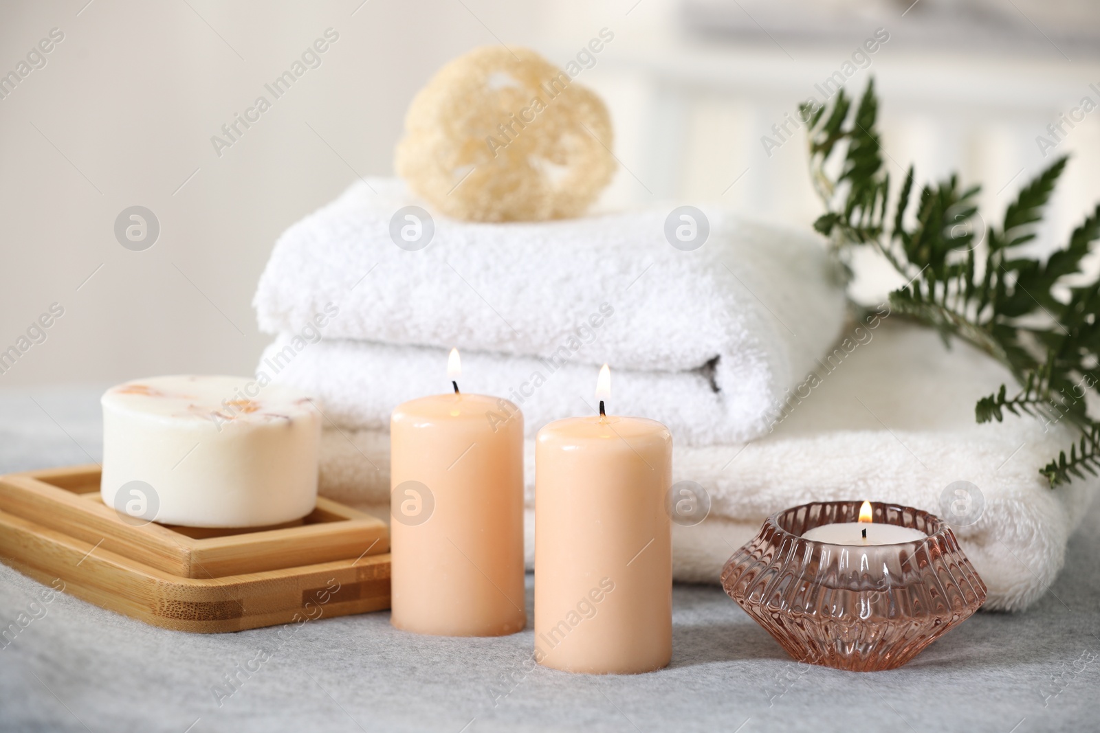 Photo of Spa composition. Burning candles, soap, towels and loofah on soft grey surface