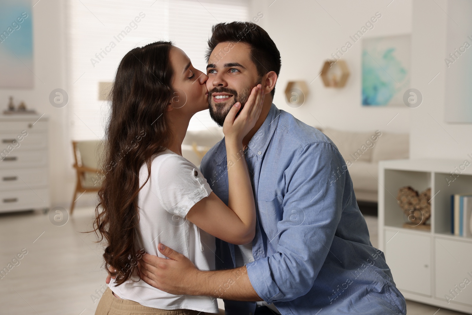 Photo of Cute couple. Woman kissing her smiling boyfriend at home