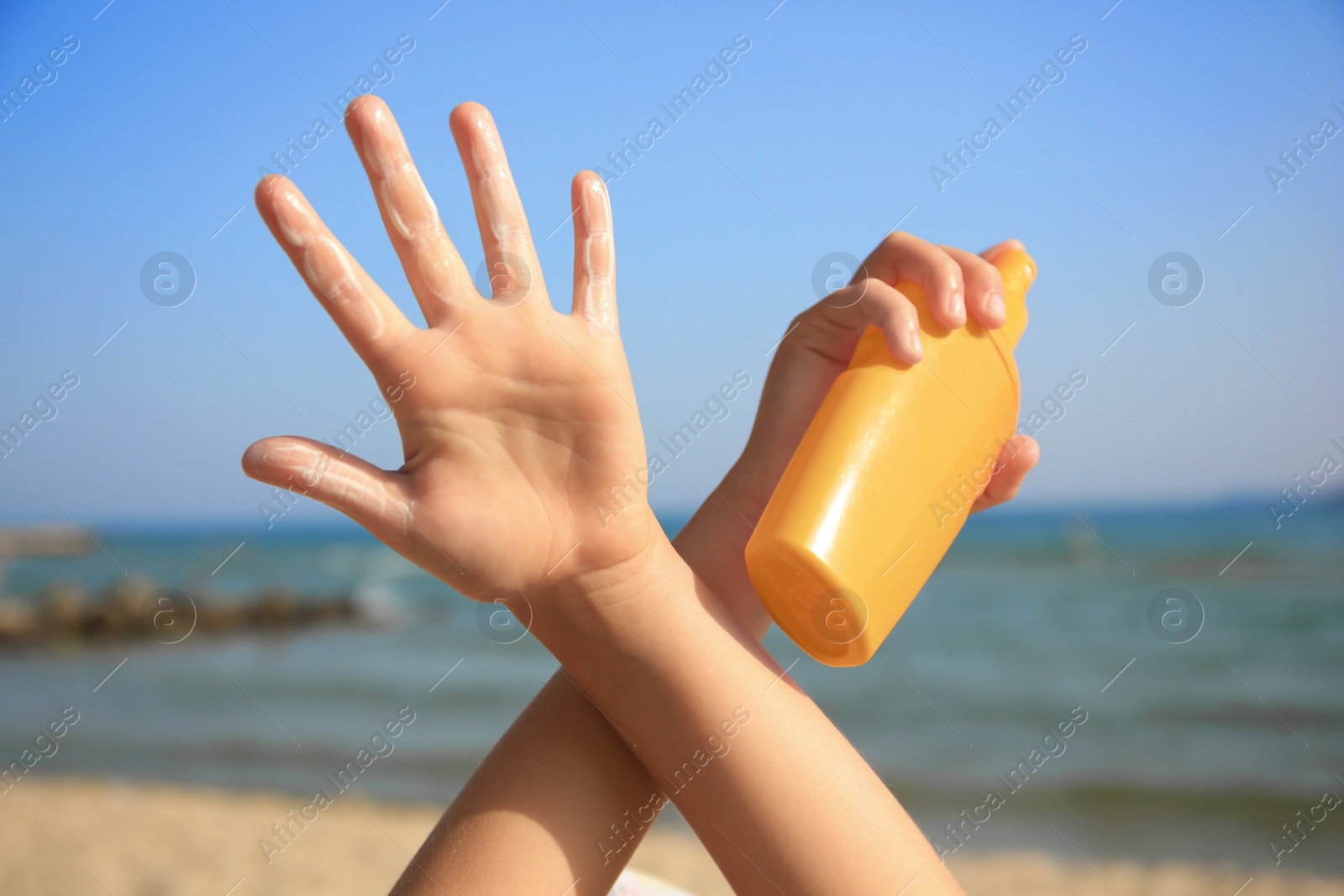 Photo of Child with bottle of sunscreen near sea, closeup. Sun protection care