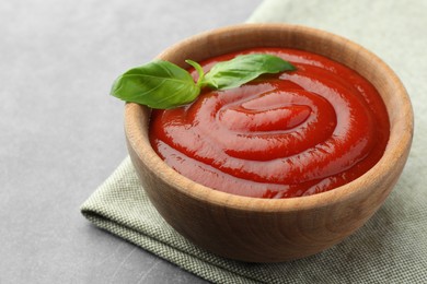 Photo of Bowl of tasty ketchup and basil on light grey table, closeup