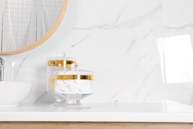 Glass jars with cotton pads and loofahs on table in bathroom. Space for text