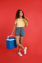 Happy young African American woman with cool box and bottle of beer on red background