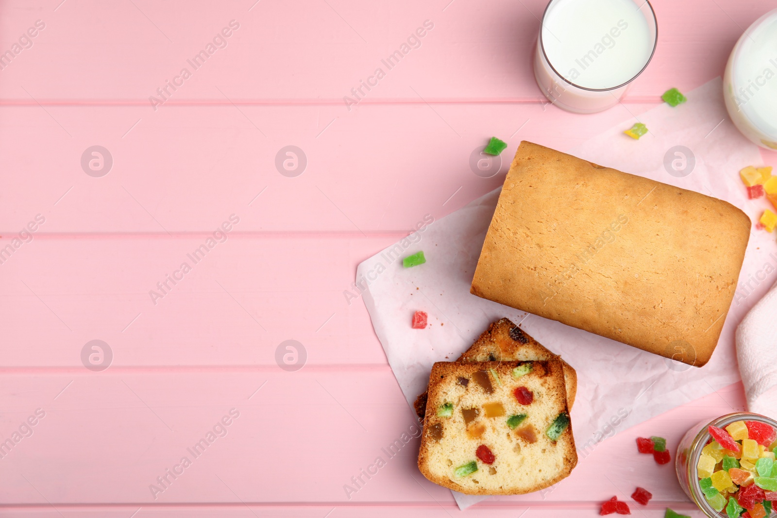 Photo of Delicious cake with candied fruits and milk on pink wooden table, flat lay. Space for text