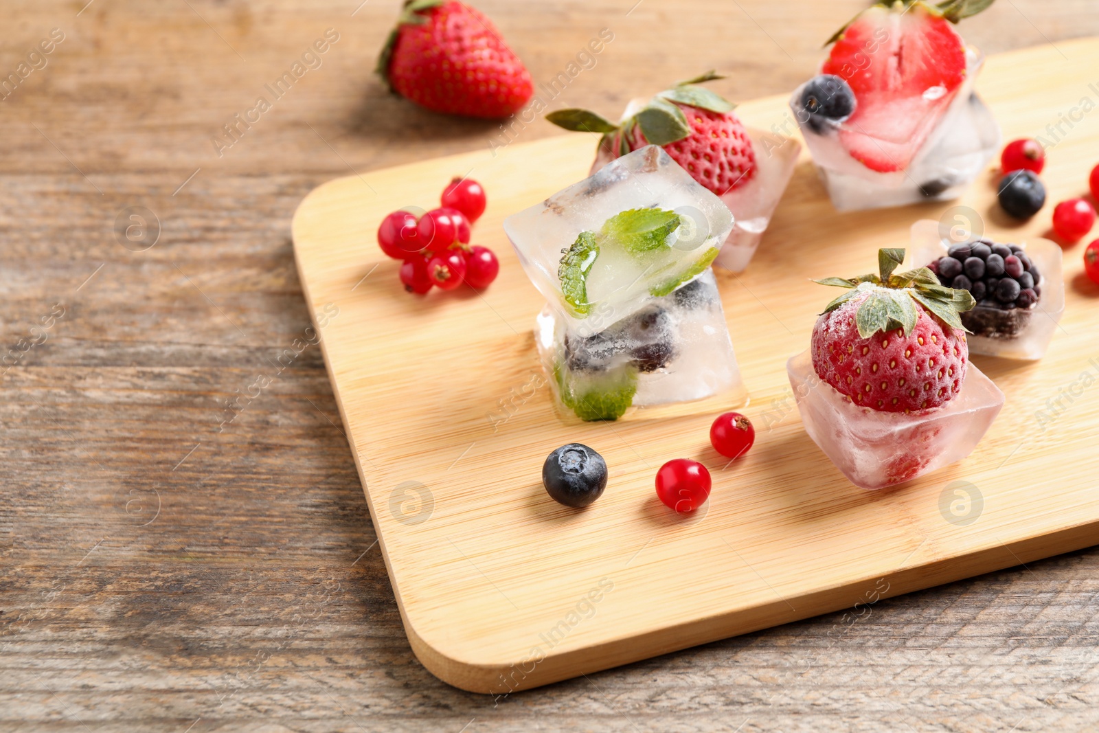 Photo of Ice cubes with different berries and mint on wooden table