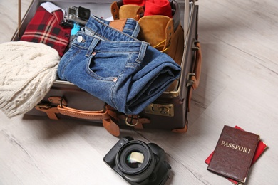 Suitcase with clothes, passports and camera on wooden floor. Winter vacation