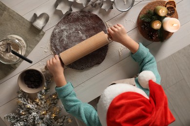 Photo of Little child rolling dough for Christmas cookies at white wooden table, top view
