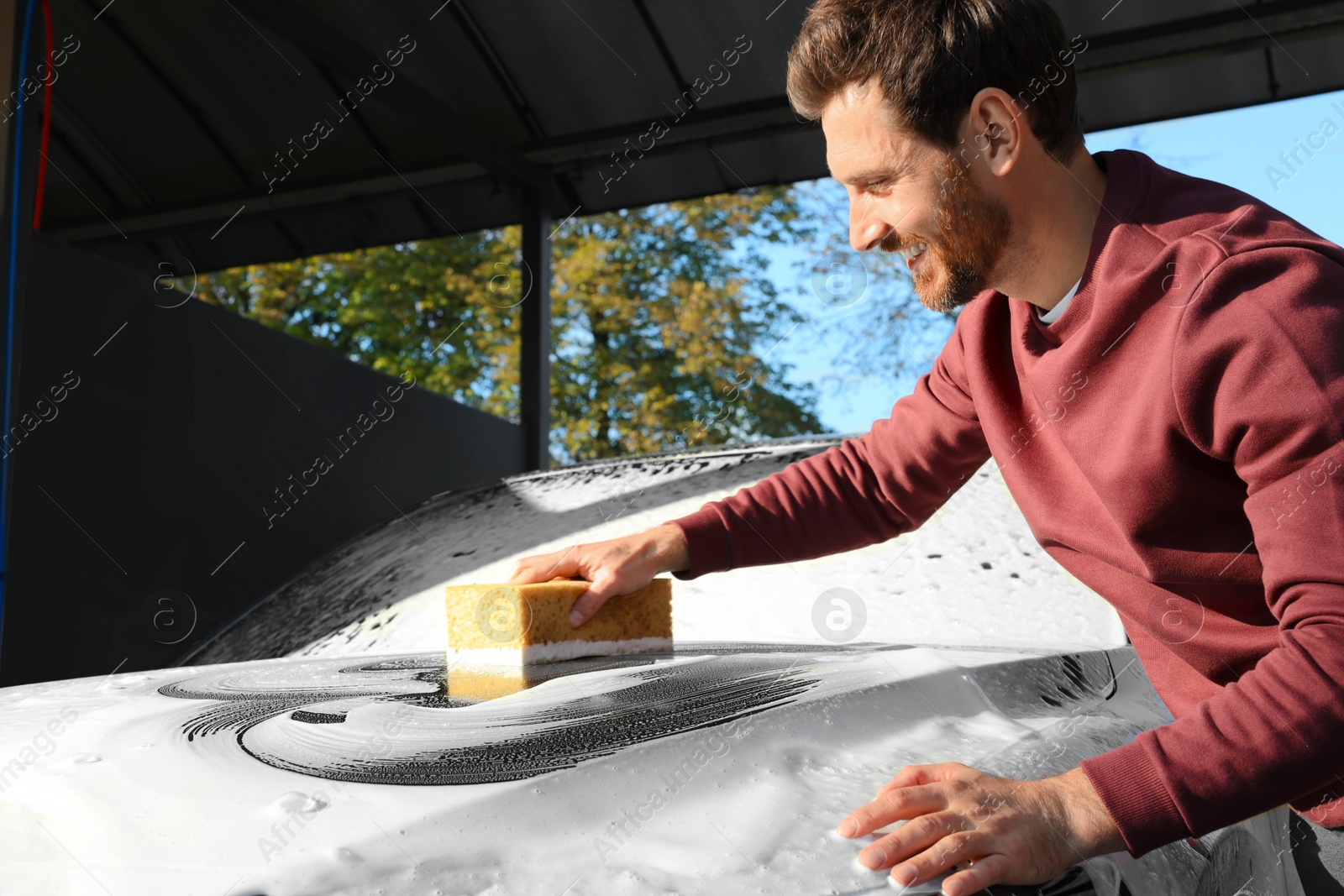 Photo of Worker washing auto with sponge at outdoor car wash