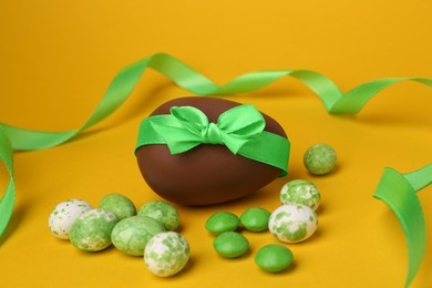 Photo of Tasty chocolate egg with green ribbon and candies on orange background