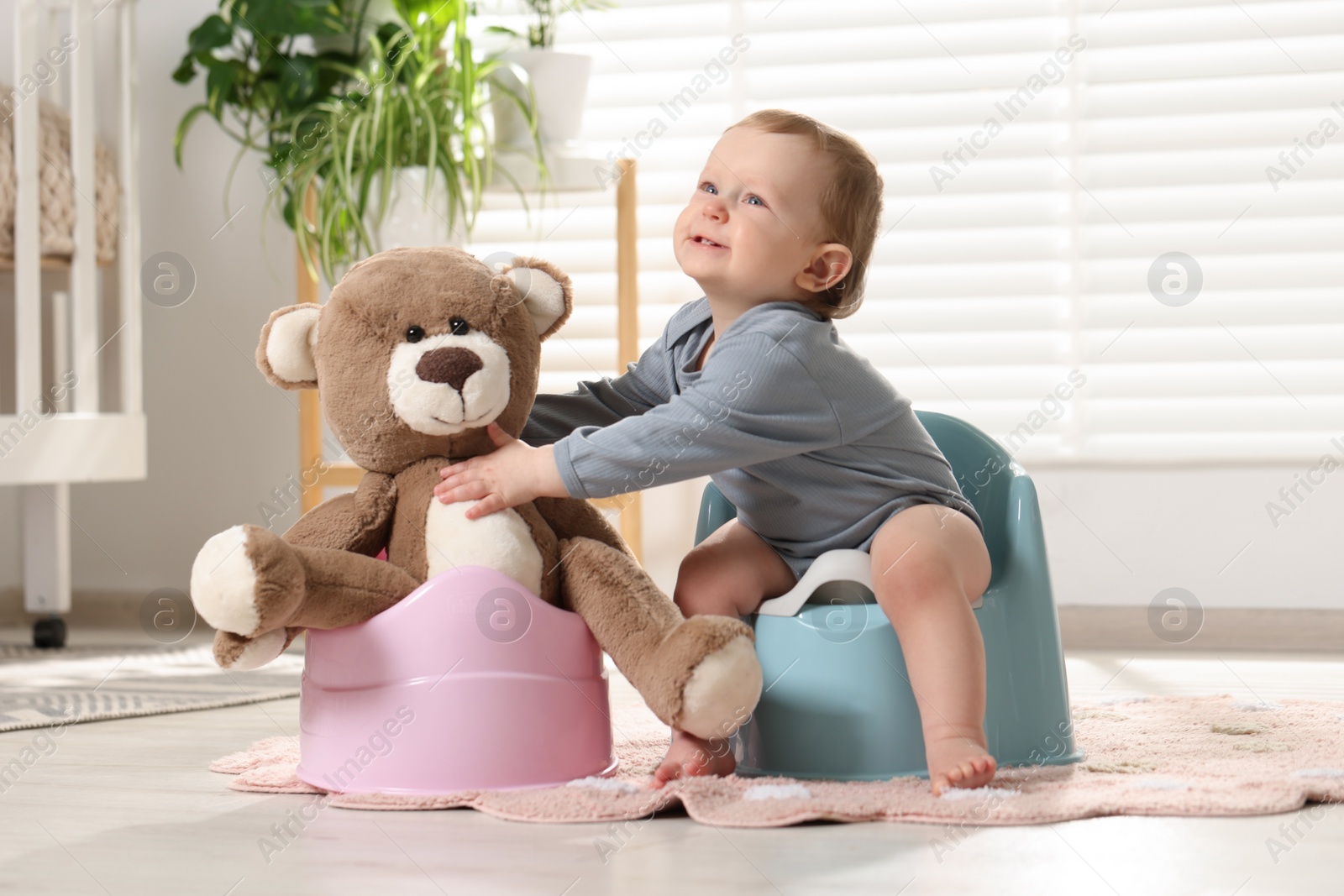 Photo of Little child and teddy bear sitting on plastic baby potties indoors