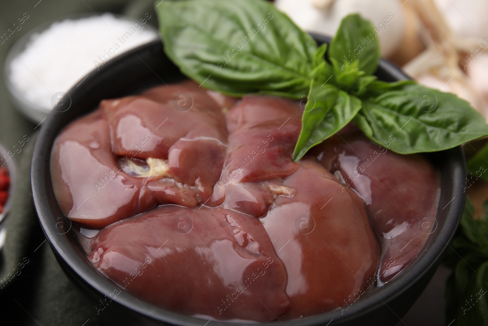 Photo of Bowl of raw chicken liver with basil on table, closeup