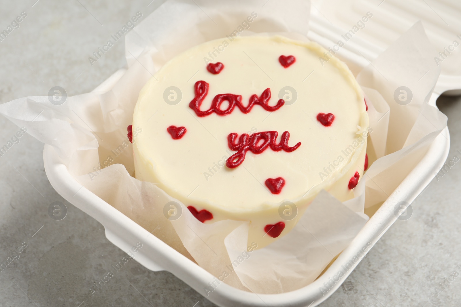 Photo of Bento cake with Love You text in takeaway box on light grey table, closeup. St. Valentine's day surprise