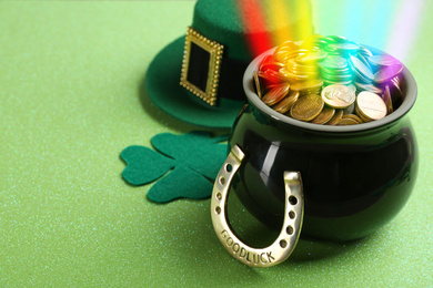 Image of Pot with gold coins, horseshoe, hat and clover on green background, space for text. St. Patrick's Day celebration