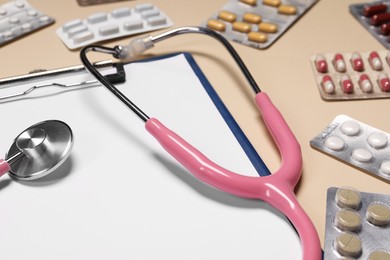 Photo of Stethoscope, clipboard and pills on beige background, closeup. Medical tool