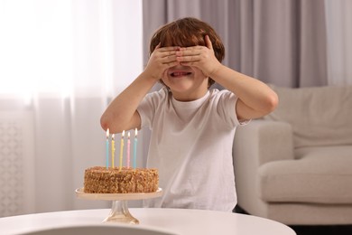 Cute boy with birthday cake at table indoors