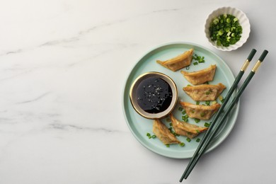 Photo of Delicious gyoza (asian dumplings) with soy sauce, green onions and chopsticks on white marble table, flat lay. Space for text