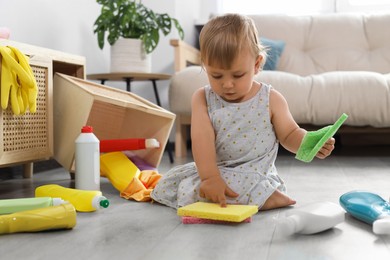 Cute baby playing with cleaning supplies on floor at home. Dangerous situation