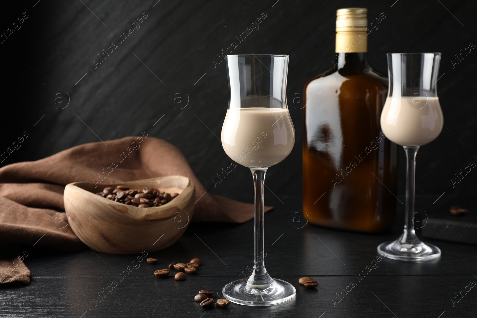 Photo of Coffee cream liqueur in glasses, bottle and beans on black wooden table