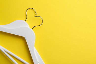 Photo of White hangers on yellow background, top view. Space for text