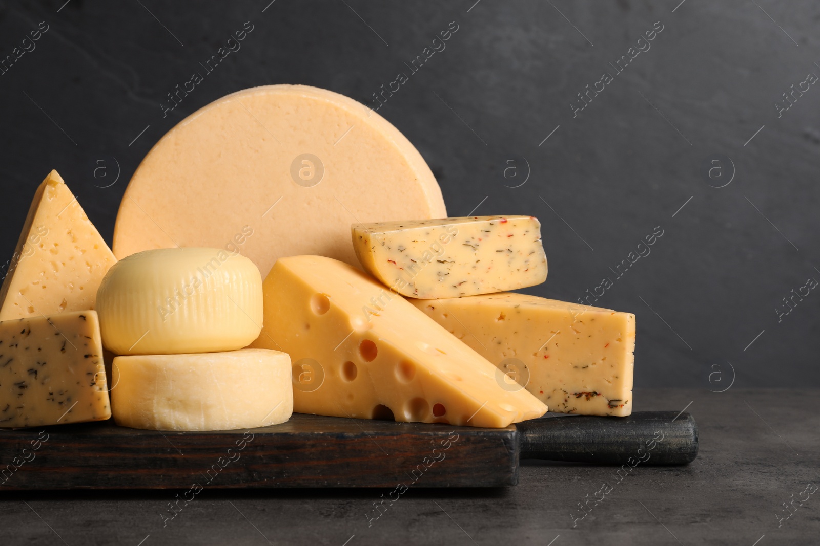 Photo of Wooden board with different sorts of cheese on grey table