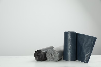 Photo of Rolls of different color garbage bags on table against light background. Space for text