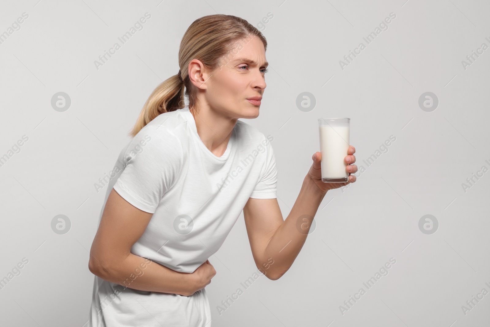 Photo of Woman with glass of milk suffering from lactose intolerance on white background