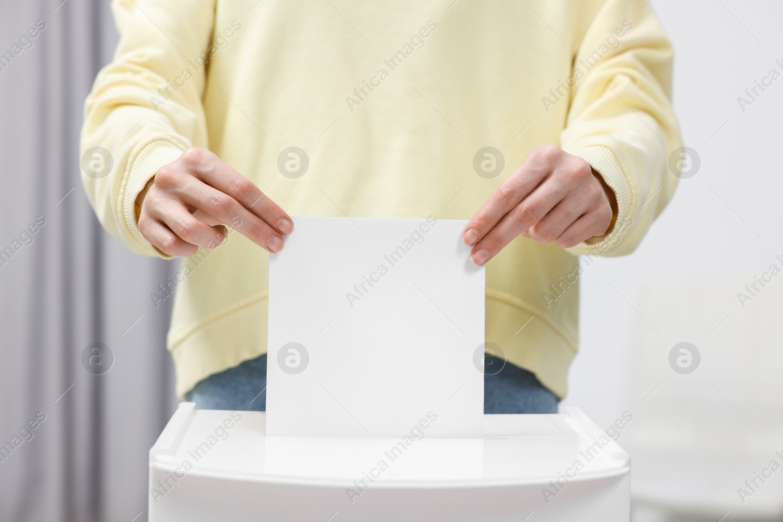 Photo of Woman putting her vote into ballot box on blurred background, closeup