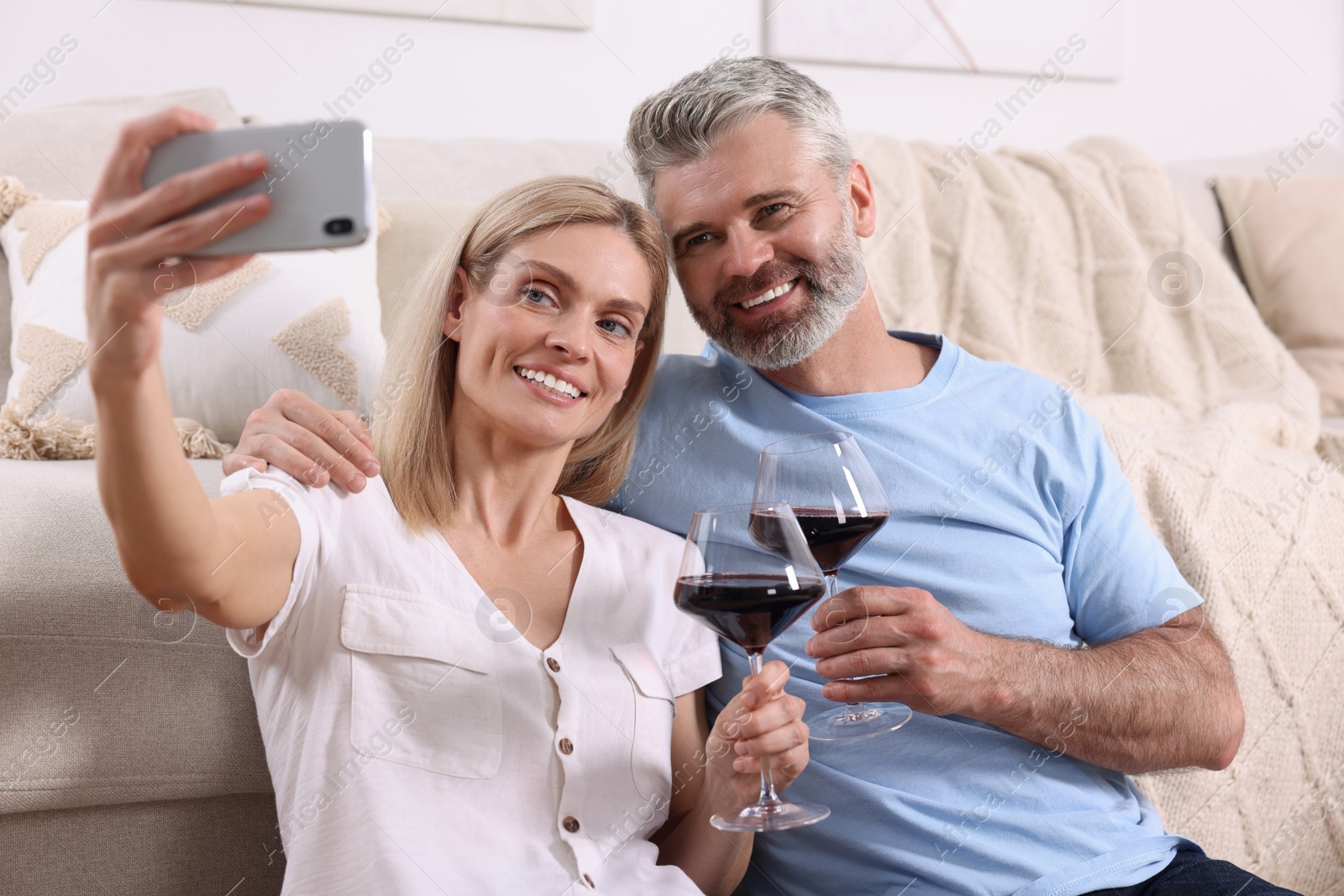 Photo of Happy affectionate couple with glasses of wine taking selfie at home. Romantic date