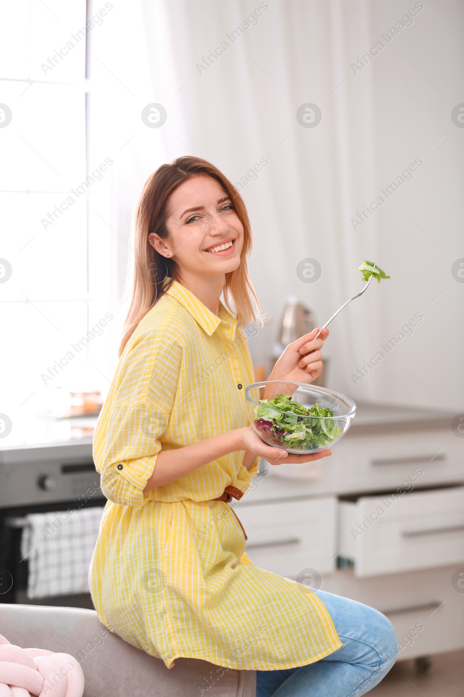 Photo of Happy young woman eating salad in kitchen. Healthy diet