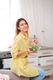 Photo of Happy young woman eating salad in kitchen. Healthy diet