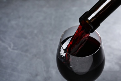 Pouring red wine from bottle into glass on grey background, closeup. Space for text