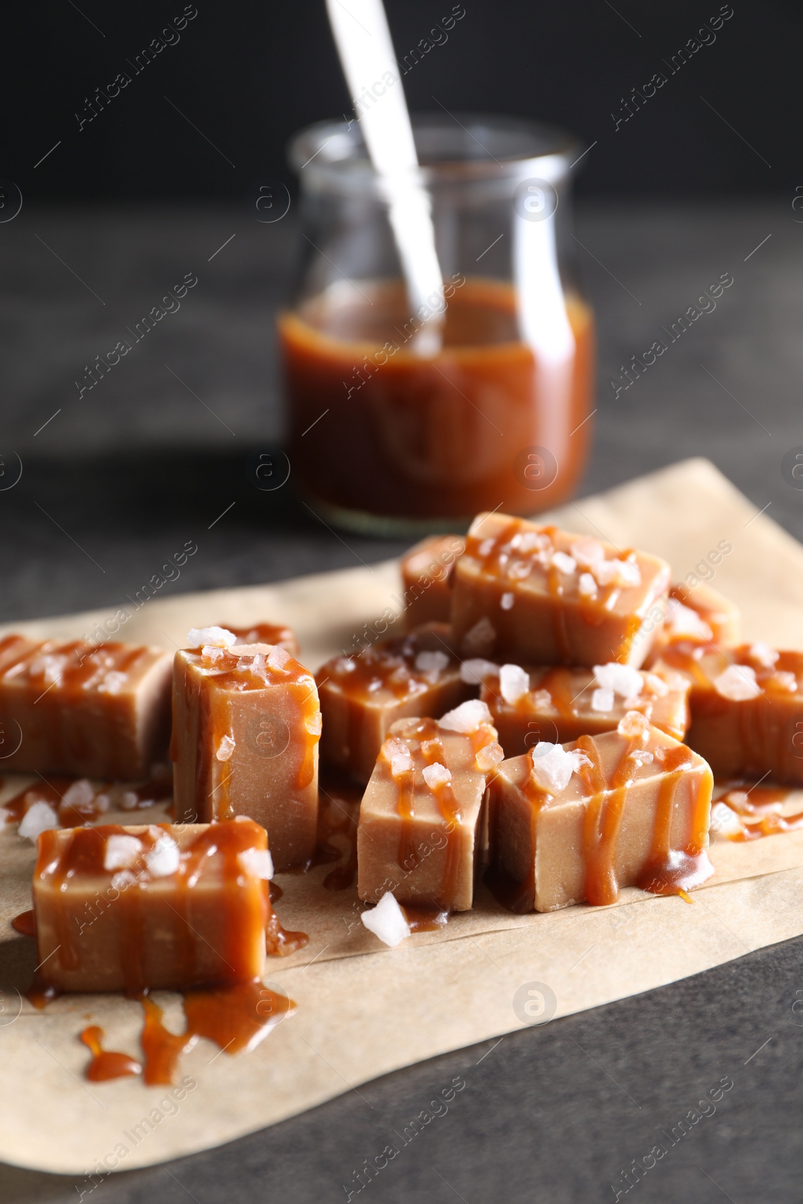 Photo of Tasty candies, caramel sauce and salt on grey table, closeup