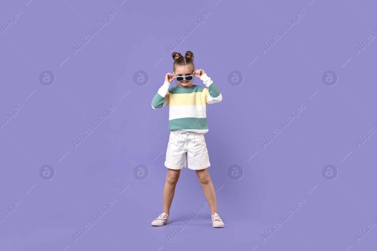 Photo of Cute little girl in sunglasses dancing on violet background