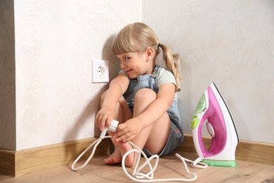 Photo of Little child playing with iron plug near electrical socket at home. Dangerous situation