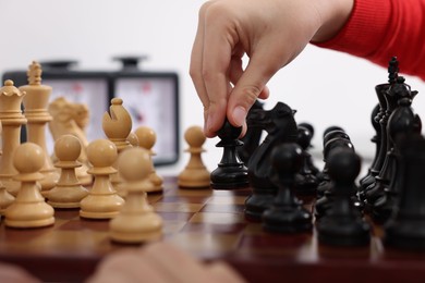 Photo of Little child playing chess at table indoors, closeup