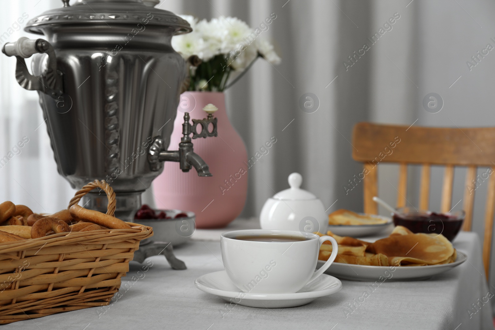 Photo of Vintage samovar, cup of hot drink and snacks served on table indoors. Traditional Russian tea ceremony