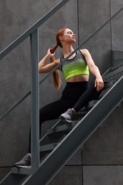 Beautiful woman in stylish gym clothes sitting on stairs on street