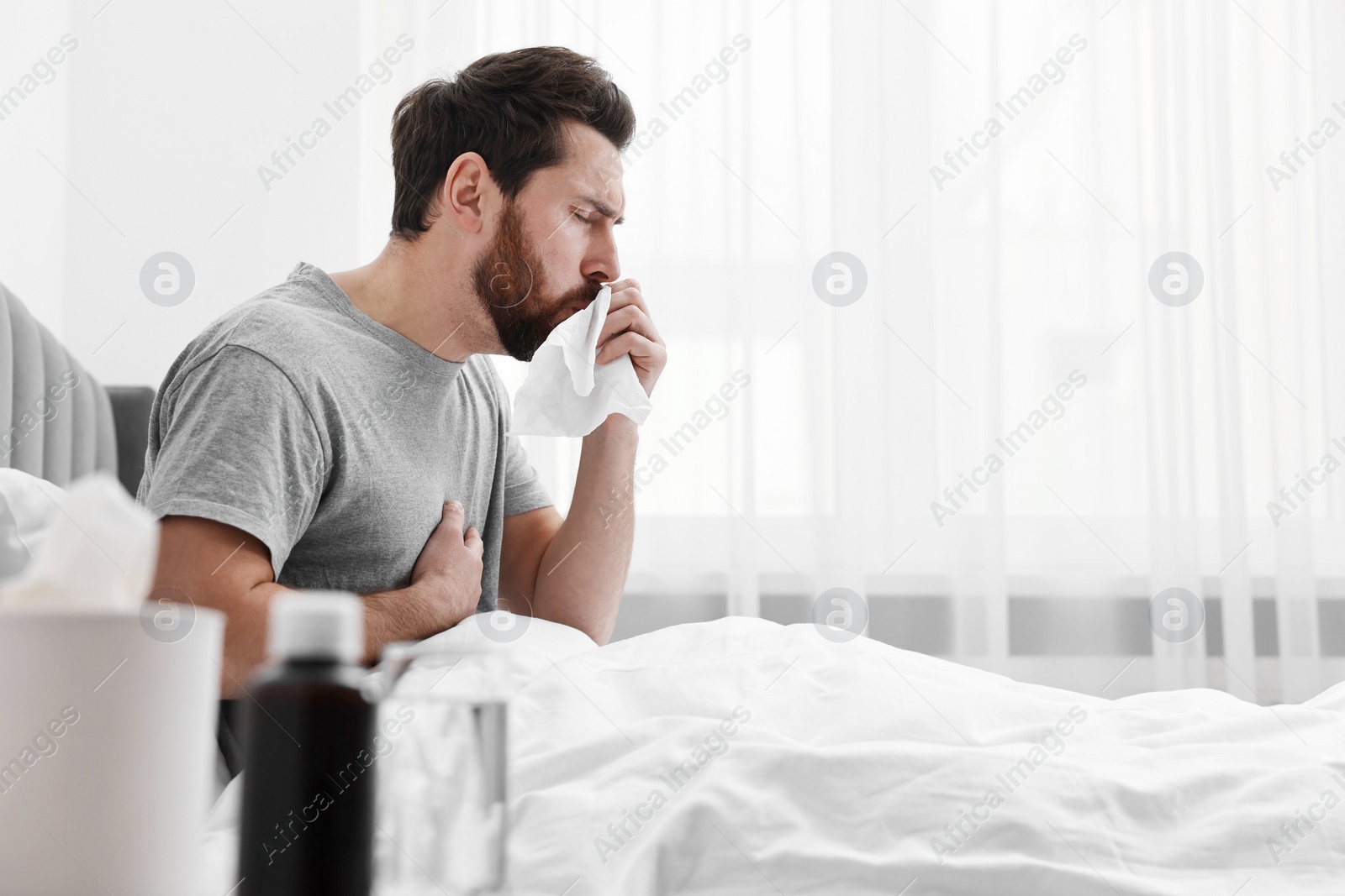 Photo of Sick man coughing on bed at home, space for text. Cold symptoms