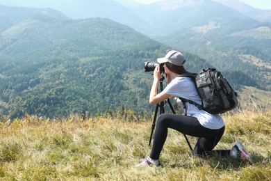 Photo of Woman taking photo of mountain landscape with modern camera on tripod outdoors