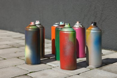 Photo of Cans of different spray paints on pavement near wall