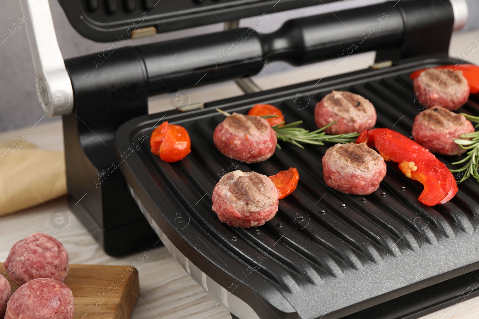 Photo of Electric grill with vegetables, meat balls and rosemary on table, closeup