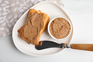 Photo of Crispy crackers with delicious meat pate and knife on white table, flat lay