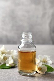 Essential oil and jasmine flowers on light grey table