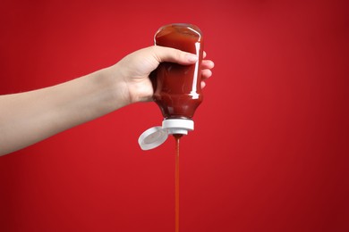 Photo of Woman pouring tasty ketchup from bottle on red background, closeup. Space for text
